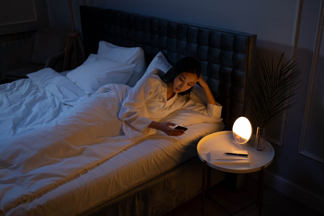 person using smartphone in bed at night illustrating what blue light does to your sleep